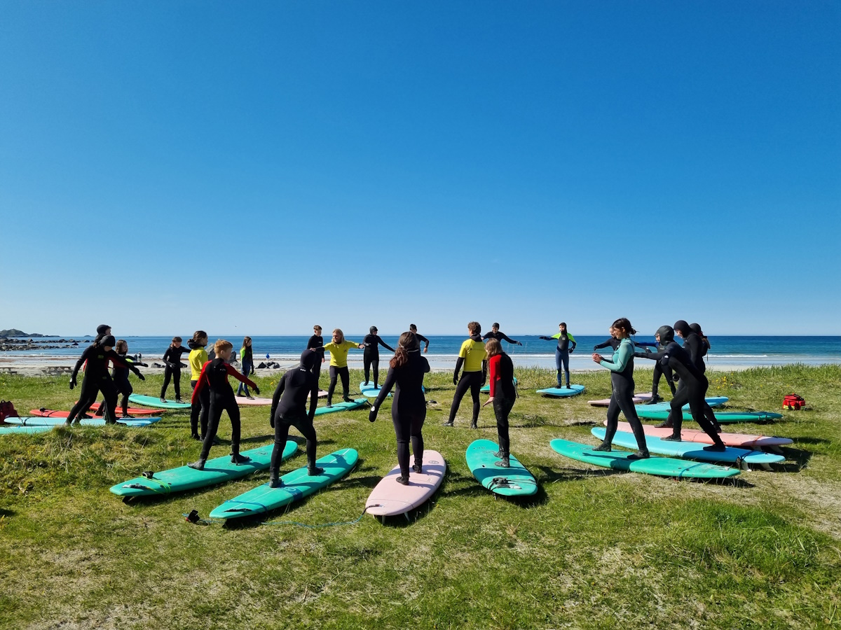 Ungdommer i surferdresser har torrtrening på Flakstad strand. Foto.